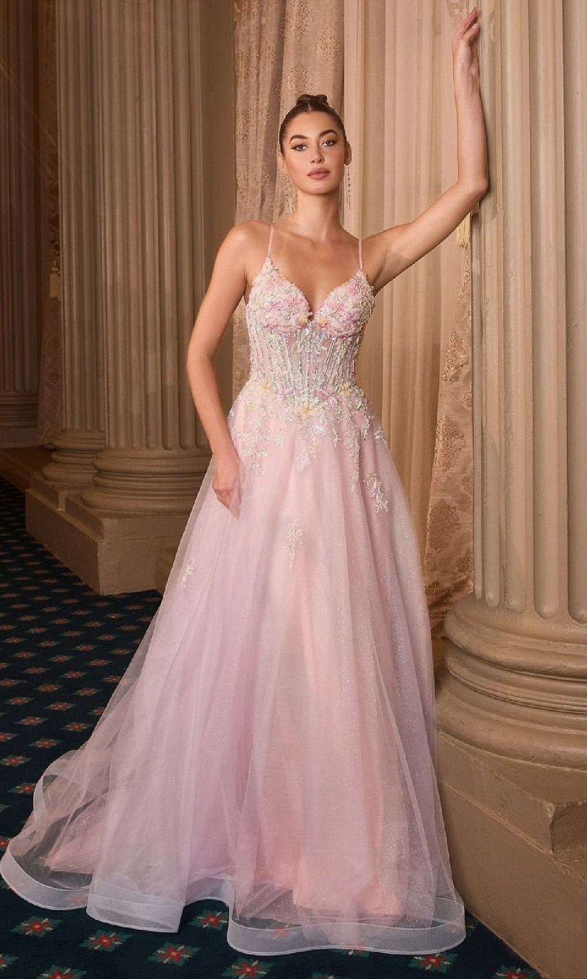 A woman wears the Classic Long Pink Prom Dress: Andrea and Leo A1477, featuring thin straps and embroidered flowers, as she stands against ornate columns and a curtain in an elegant interior.